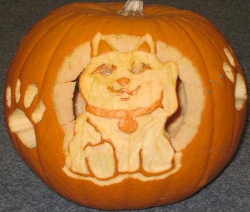 A pumpkin carved with the image of a smiling cat wearing a collar, with cat paw prints on each side.