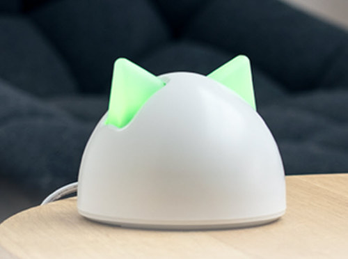 A dome-shaped white device with glowing green cat ears sitting on a wooden surface.